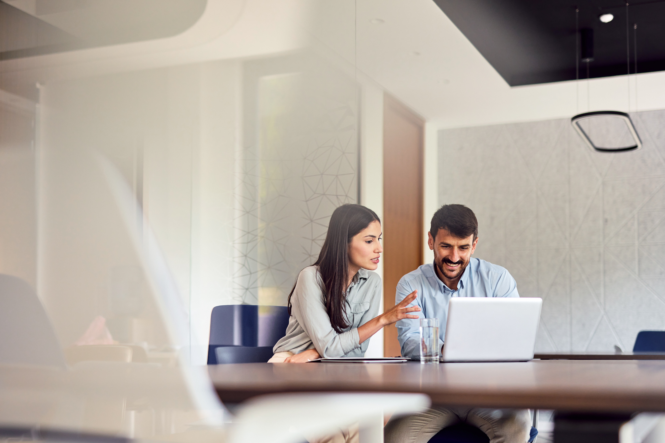 Two young professionals collaborating on a project, engaging with a laptop and exchanging ideas in a bright, modern office space filled with energy and creativity